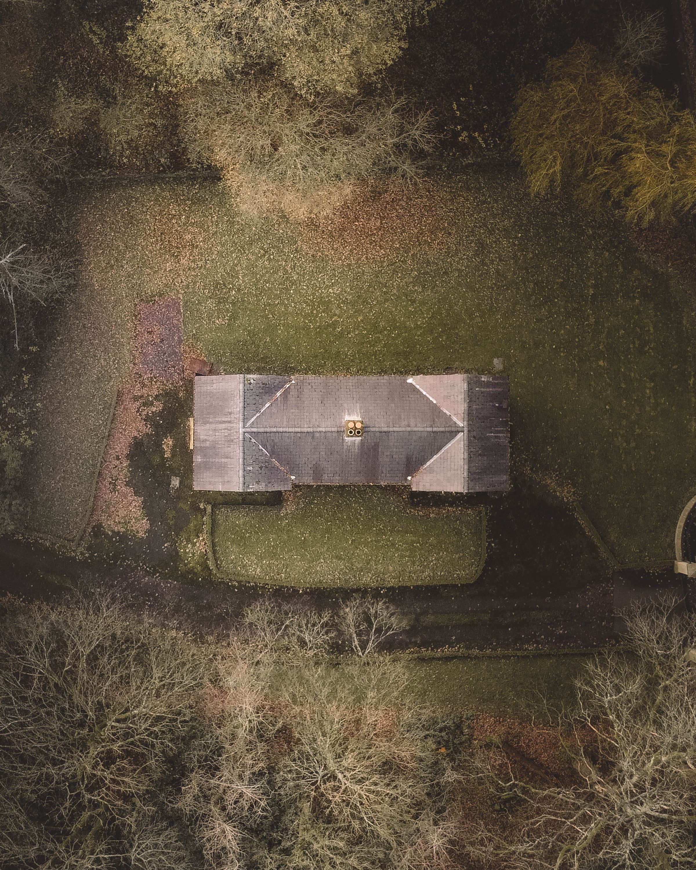 Aerial view straight down on a house with a hip roof, surrounded by lawn and autumn trees