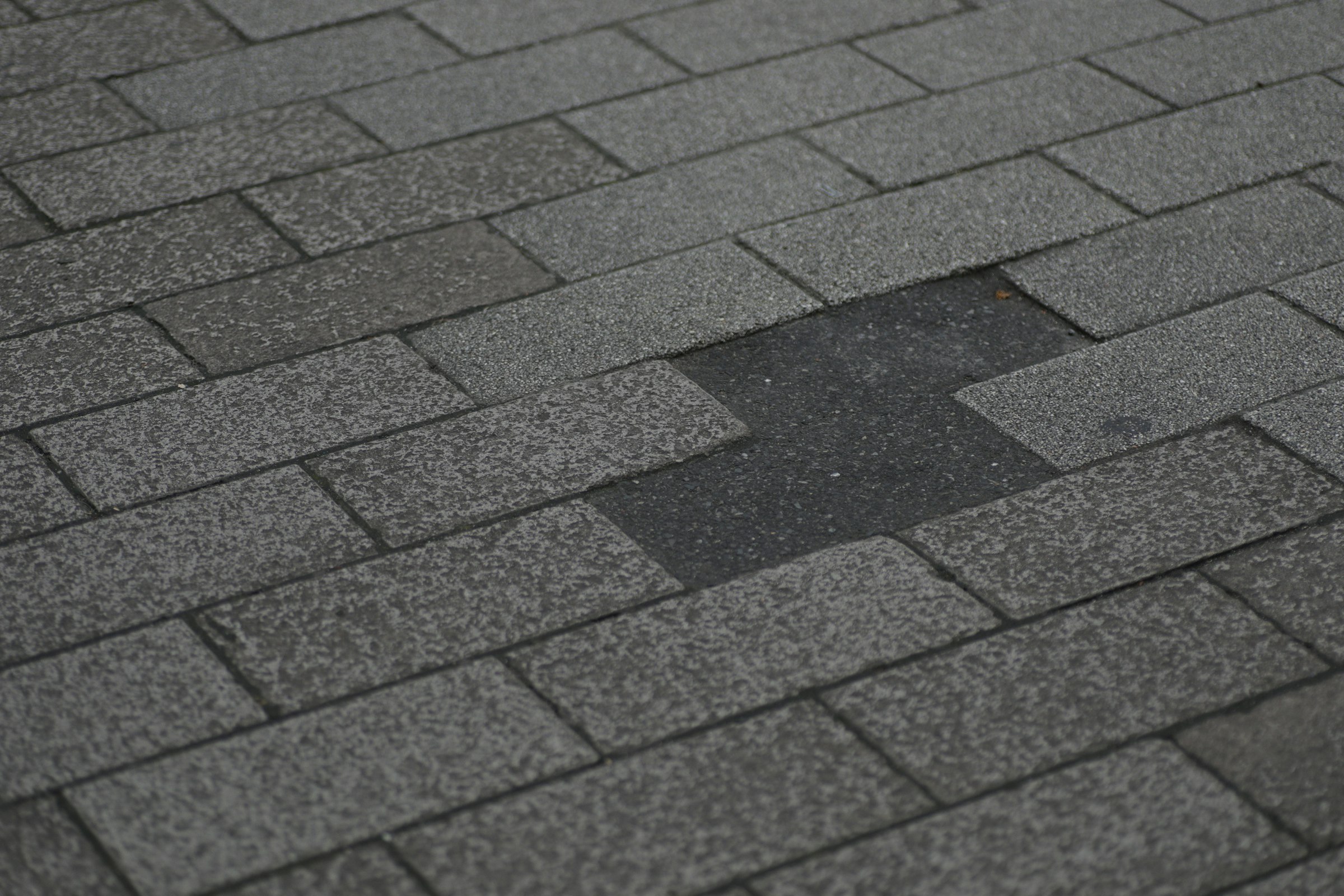 A grey asphalt shingle roof with a patch of missing shingles exposing the darker layer beneath